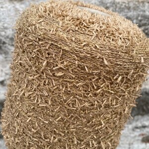 May include: A close-up of a beige yarn with a fuzzy texture. The yarn is tightly wound into a ball shape.