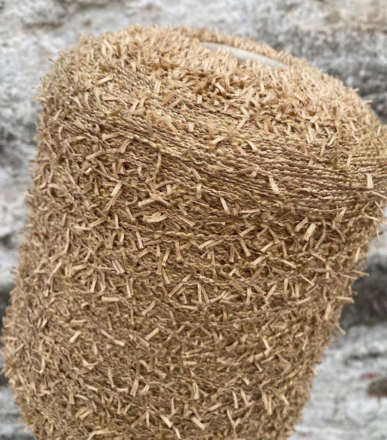 May include: A close-up of a beige yarn with a fuzzy texture. The yarn is tightly wound into a ball shape.