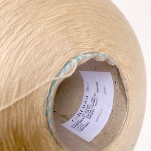May include: A beige ball of yarn with a blue and white striped label. The label reads "CARIAGGI CASHMERE 100 Nm. 2/28 100%WS Partita PCKA000 22660 COSMETIC C85603 Bagno 000000 22660 30/08/2022".