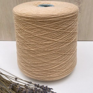May include: A skein of beige yarn wound on a cardboard spool. The yarn is soft and natural looking, perfect for knitting or crocheting.