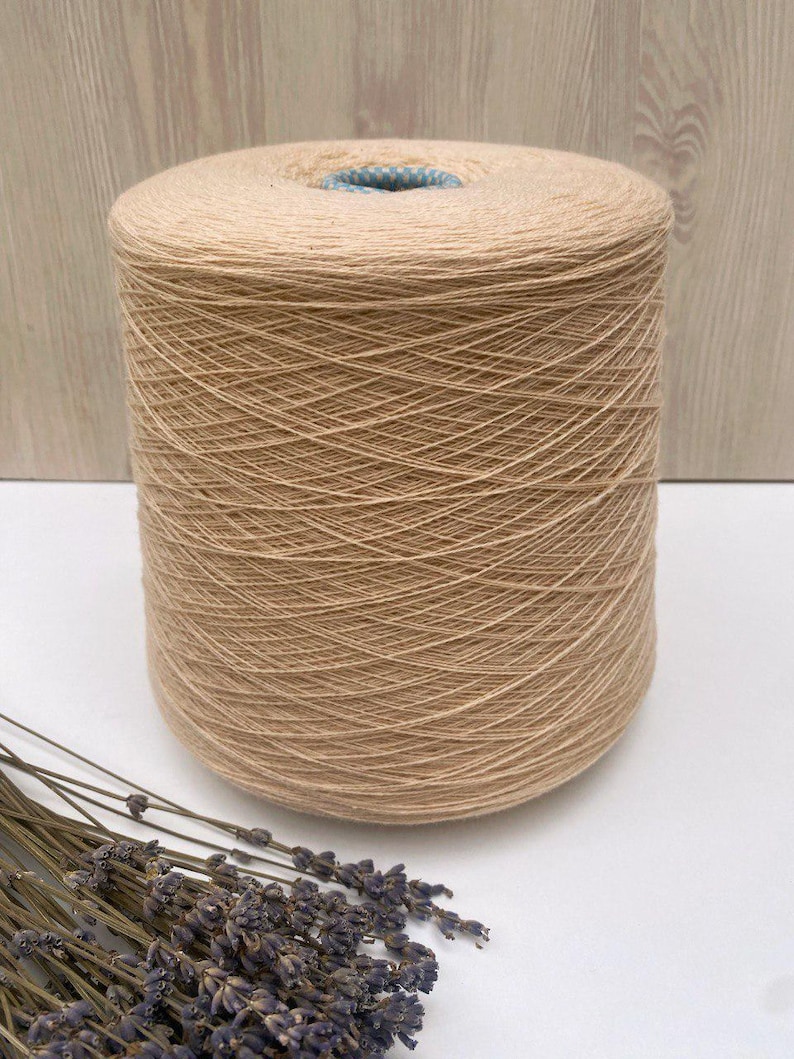 May include: A skein of beige yarn wound on a cardboard spool. The yarn is soft and natural looking, perfect for knitting or crocheting.