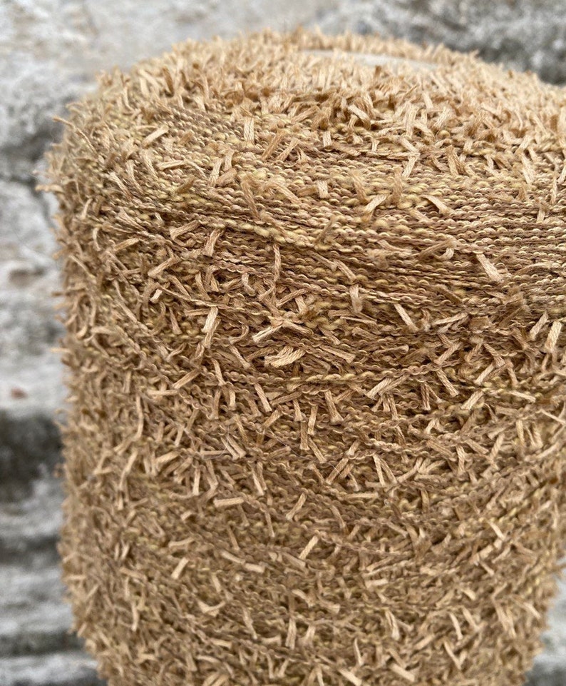 May include: Close-up of a beige yarn with a fuzzy texture. The yarn is tightly wound into a ball shape.