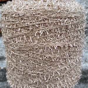 May include: A skein of beige yarn with a fuzzy texture. The yarn is wound around a cardboard spool.