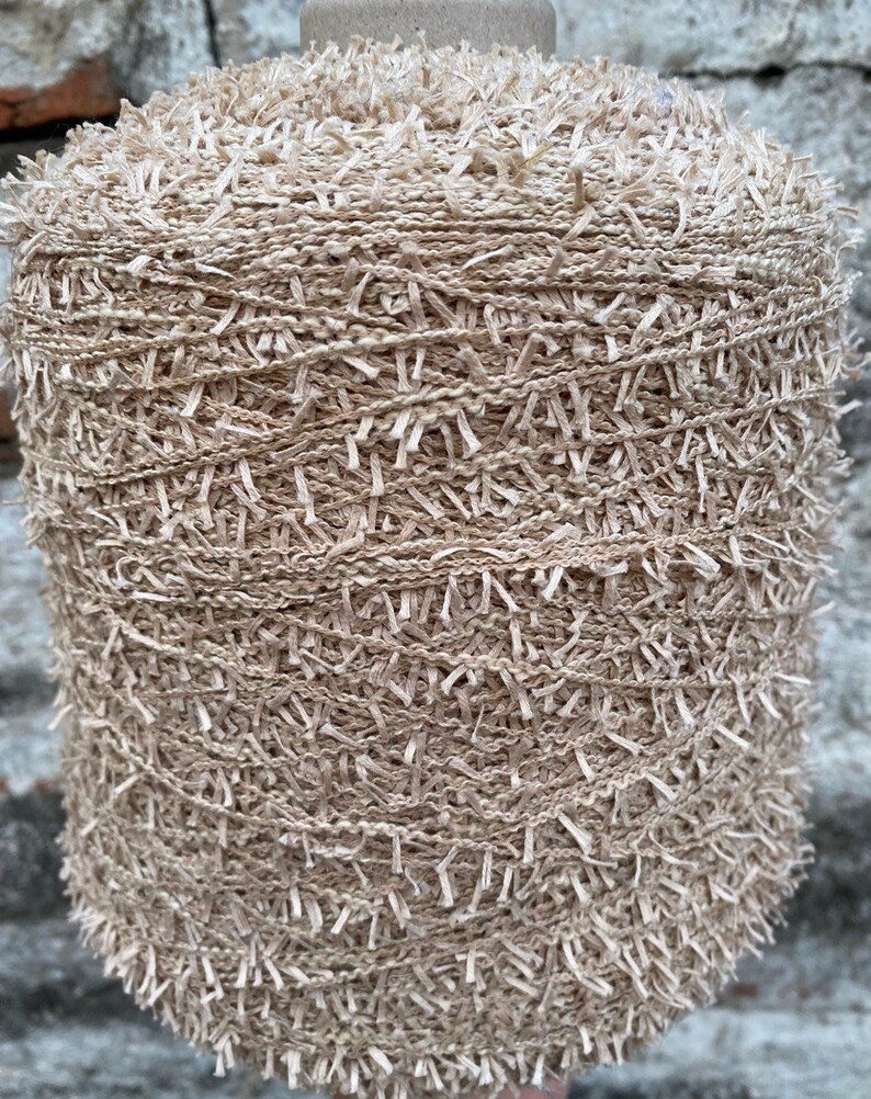 May include: A skein of beige yarn with a fuzzy texture. The yarn is wound around a cardboard spool.