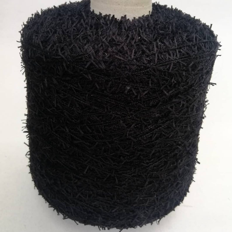 May include: A spool of black yarn with a fuzzy texture. The yarn is tightly wound and has a rough, uneven surface.