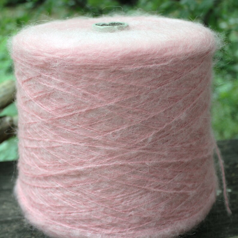 Op de afbeelding: Een roze garenklos, gewikkeld op een kartonnen spoel. Het garen is zacht en pluizig, met een delicate roze tint.