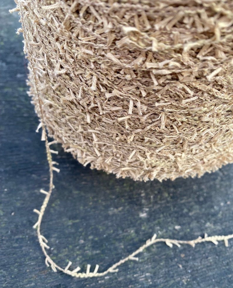 May include: A close-up of a ball of beige yarn with a fuzzy texture. The yarn is unraveling and creating a long strand.