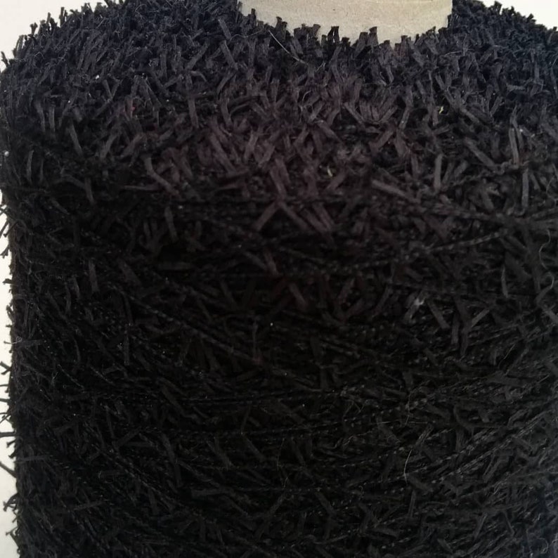 May include: Close-up of black yarn with a fuzzy texture. The yarn is tightly wound into a ball.