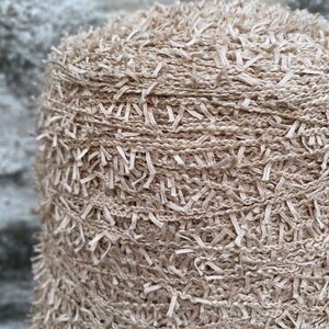 May include: Close-up of a beige yarn with a fuzzy texture. The yarn is wound into a ball and is ready for knitting or crocheting.