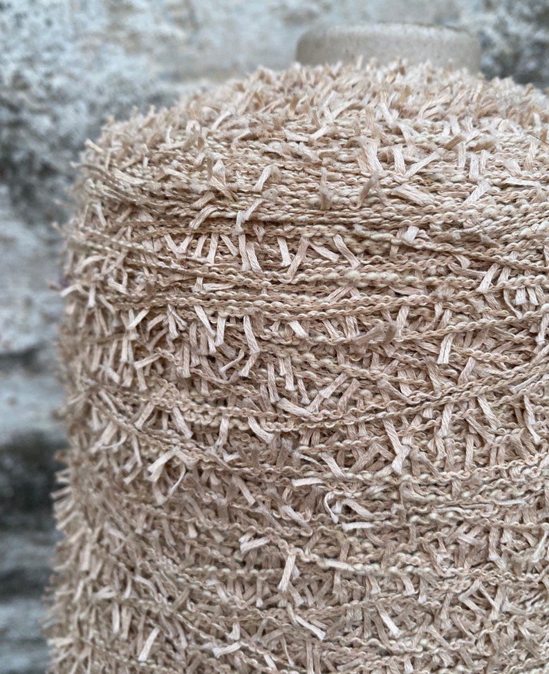 May include: Close-up of a beige yarn with a fuzzy texture. The yarn is wound into a ball and is ready for knitting or crocheting.
