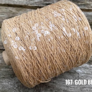 May include: A spool of beige yarn with white sequins woven throughout. The spool is labeled "167 - GOLD BEIGE".