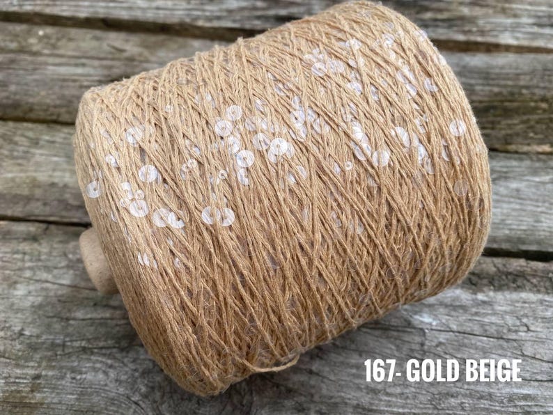 May include: A spool of beige yarn with white sequins woven throughout. The spool is labeled "167 - GOLD BEIGE".