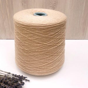 May include: A large spool of beige yarn. The yarn is wound tightly around the spool and has a smooth, even texture.