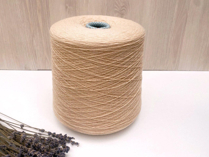 May include: A large spool of beige yarn. The yarn is wound tightly around the spool and has a smooth, even texture.