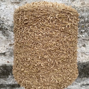 May include: A close-up of a spool of brown yarn with a fuzzy texture. The yarn is made of natural fibers and has a rustic look.