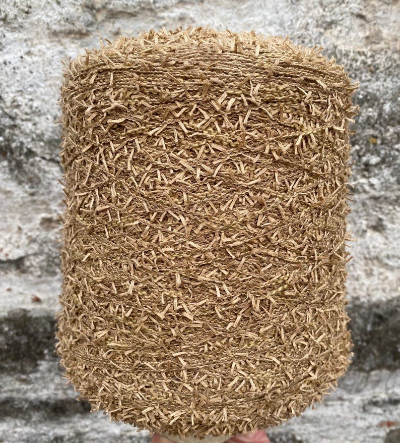 May include: A close-up of a spool of brown yarn with a fuzzy texture. The yarn is made of natural fibers and has a rustic look.
