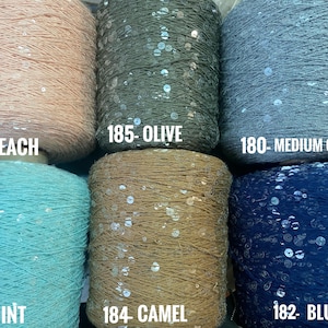 May include: Six spools of yarn with sequins, in colors peach, olive, medium gray, mint, camel, and blue. Each spool has a label with a number and color name.