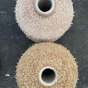 May include: Two spools of yarn, one beige and one brown, with a textured, fuzzy surface. The spools are stacked on top of each other.