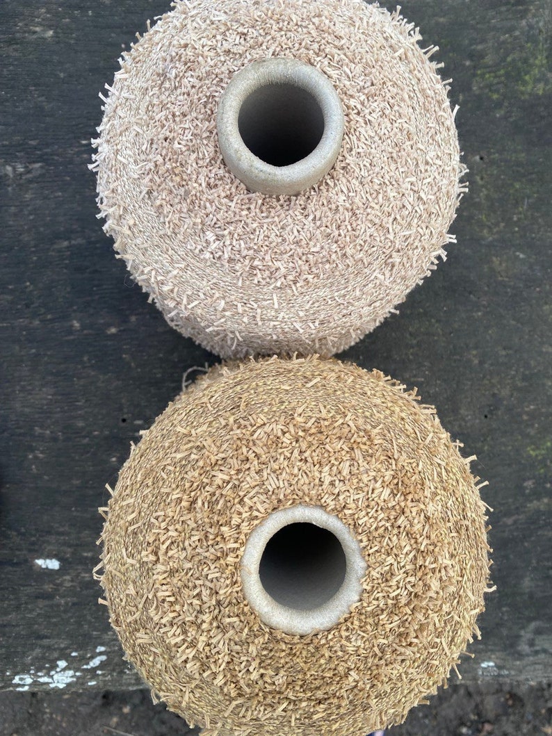 May include: Two spools of yarn, one beige and one brown, with a textured, fuzzy surface. The spools are stacked on top of each other.