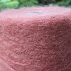 Op de afbeelding: Een bol zachte, pluche garen in een stoffige roze kleur. Het garen is gewikkeld rond een kartonnen buis.