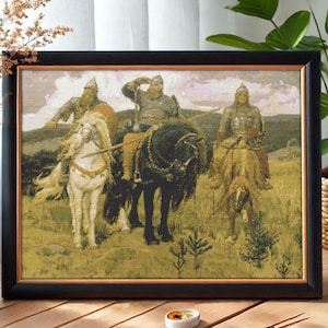 May include: A cross-stitch embroidery depicting three figures on horseback, wearing medieval armour and riding through a grassy landscape. The figures are riding white, black, and brown horses. The embroidery is framed in a black frame.