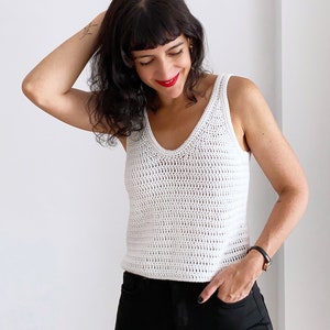 Woman wearing a handmade white crochet tank top created using the Top Cora pattern. This crochet pattern is designed for women, featuring a summer-friendly lightweight DK yarn and a modern tank top style. Perfect for casual outfits or summer layering