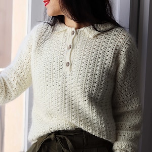 May include: A white crocheted sweater with a collared neckline and a button closure. The sweater has a loose fit and long sleeves.