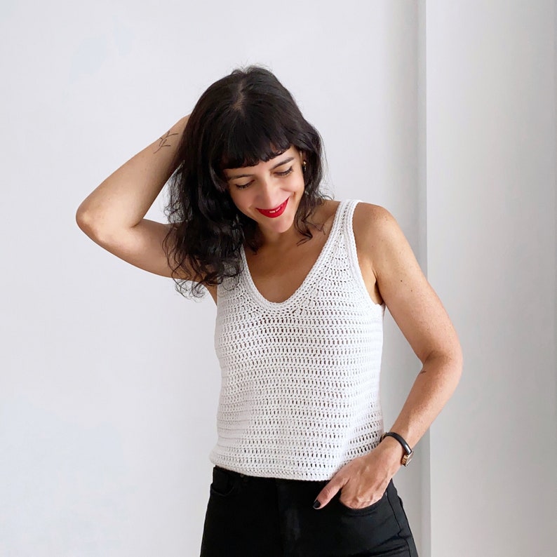 Woman wearing a handmade white crochet tank top created using the Top Cora pattern. This crochet pattern is designed for women, featuring a summer-friendly lightweight DK yarn and a modern tank top style. Perfect for casual outfits or summer layering