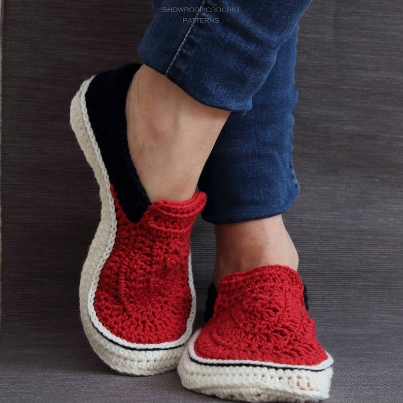 May include: Red, white, and black crocheted slippers with a casual, slip-on style. The slippers have a white trim around the sole and a black stripe on the back.