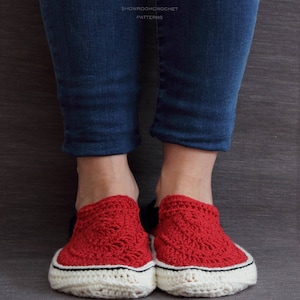 May include: Red crochet slippers with white trim and black accents. The slippers are worn by a person wearing blue jeans.