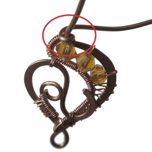 Peut inclure: Gros plan d'un pendentif en fil de cuivre en forme de c&oelig;ur avec une boucle en haut. Le pendentif est d&eacute;cor&eacute; de petites perles de verre transparentes et d'un enroulement de fil de cuivre. Le fil est torsad&eacute; en haut pour cr&eacute;er une boucle permettant d'attacher une cha&icirc;ne.