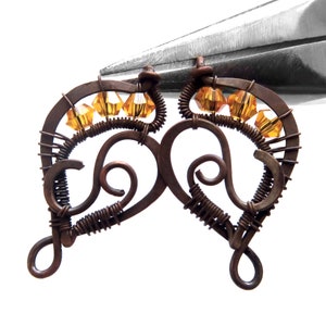 Peut inclure: Une paire de boucles d'oreilles en fil de cuivre avec un design en forme de c&oelig;ur et des cristaux de couleur ambre.