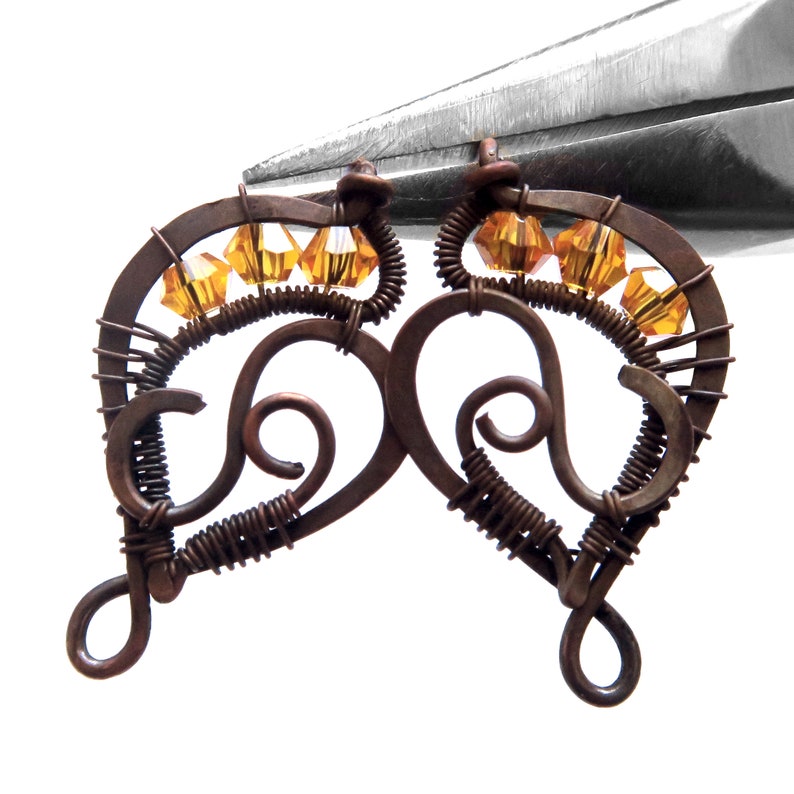 Peut inclure: Une paire de boucles d'oreilles en fil de cuivre avec un design en forme de c&oelig;ur et des cristaux de couleur ambre.