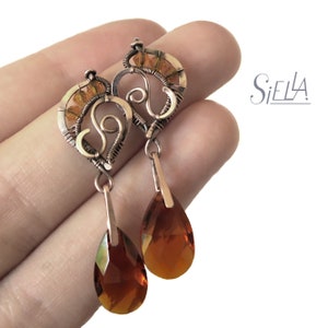 Peut inclure: Une paire de boucles d'oreilles pendantes avec un motif en forme de c&oelig;ur orn&eacute; d'un tourbillon et de perles de couleur ambre. Les boucles d'oreilles sont en fil de cuivre et ont un cristal ambre en forme de larme suspendu &agrave; chaque c&oelig;ur.