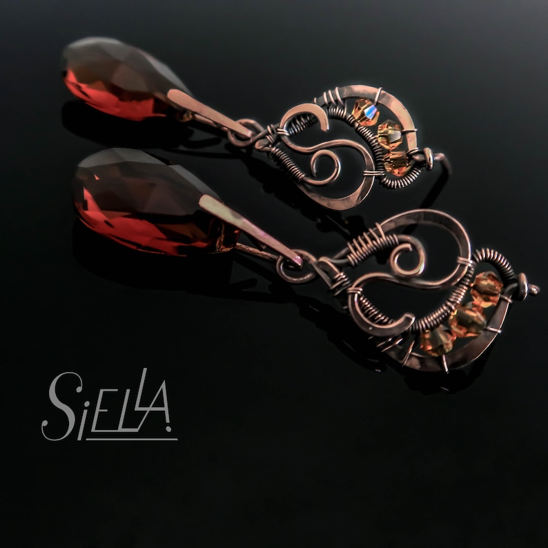 Peut inclure: Une paire de boucles d'oreilles pendantes avec un design en fil de cuivre et une pierre pr&eacute;cieuse ambr&eacute;e en forme de larme. Les boucles d'oreilles pr&eacute;sentent un motif en spirale avec de petits cristaux ambr&eacute;s.