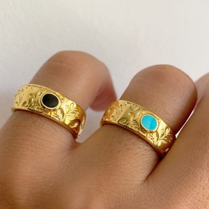 May include: Two gold rings with ornate designs. One ring has a black stone and the other has a turquoise stone.