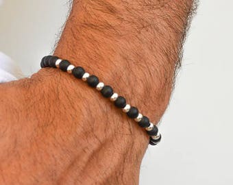 Pode incluir: Uma pulseira de contas pretas e prateadas no pulso de uma pessoa.
