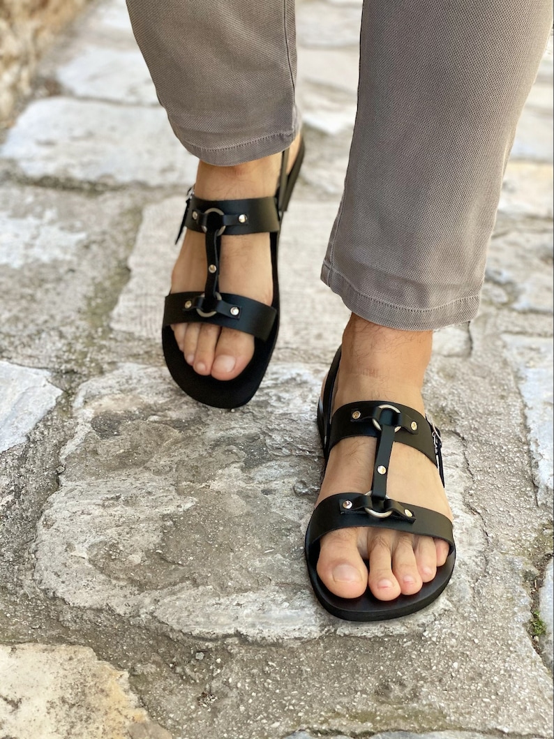 May include: Black leather sandals with multiple straps and silver buckles. The sandals have a closed toe and a flat sole.