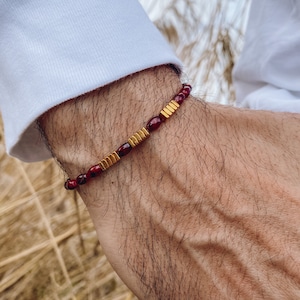 May include: A red and gold beaded bracelet with a simple design. The bracelet is worn on a person's wrist.