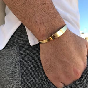 May include: A gold-colored metal bracelet with a curved design. The bracelet is worn on a person's wrist.