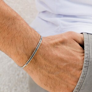 May include: A silver bracelet with a row of black stones around the band.