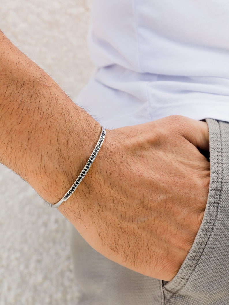 May include: A silver bracelet with a row of black stones around the band.