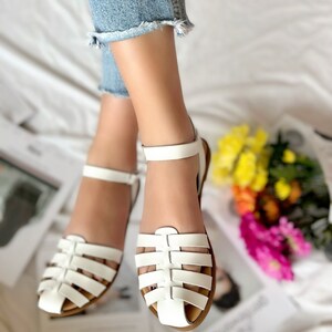 Puede incluir: Sandalias blancas de cuero con un dise&ntilde;o enjaulado y una correa de tobillo. Las sandalias tienen una suela marr&oacute;n.