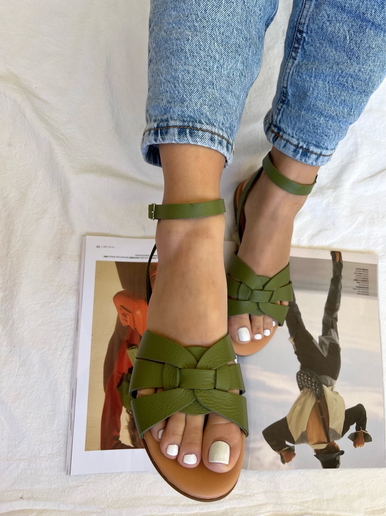 Puede incluir: Un par de sandalias de cuero verde oliva con un dise&ntilde;o de tiras cruzadas. Las sandalias tienen un cierre de hebilla en el tobillo y una suela de cuero marr&oacute;n.