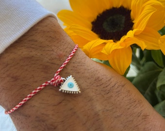 May include: Red and white string bracelet with a silver charm in the shape of a triangle with a blue eye inside.