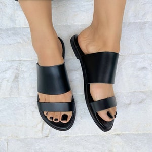 May include: Black leather sandals with two straps across the foot. The sandals have a simple design and are perfect for summer.