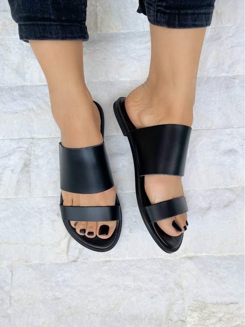 May include: Black leather sandals with two straps across the foot. The sandals have a simple design and are perfect for summer.
