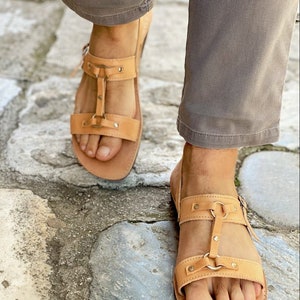May include: Tan leather sandals with two straps and a buckle closure. The sandals have a  distressed look and are adorned with small metal studs.