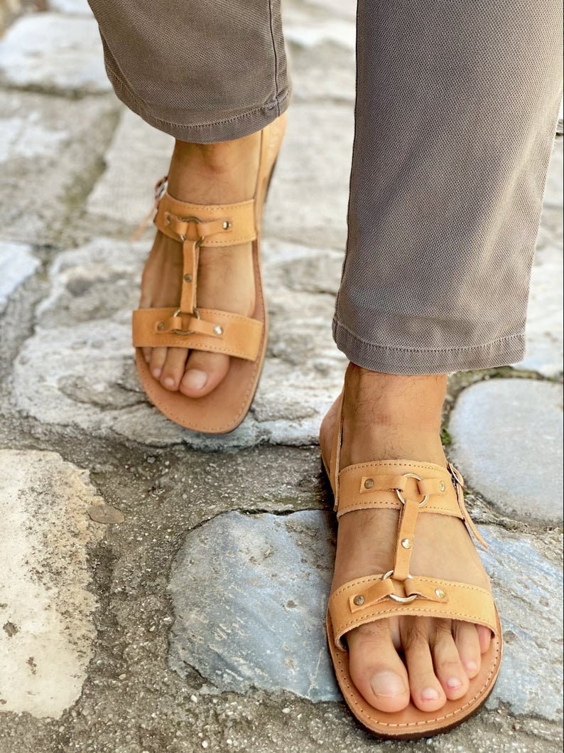 May include: Tan leather sandals with two straps and a buckle closure. The sandals have a  distressed look and are adorned with small metal studs.