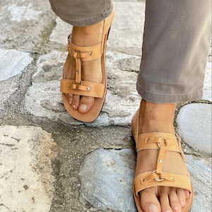 Puede incluir: Un par de sandalias de cuero marr&oacute;n con m&uacute;ltiples correas y hebillas. Las sandalias tienen la punta cerrada y una suela gruesa.